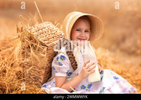 Un ritratto di una ragazza felice in un campo di grano al tramonto. Un bambino tiene in mano un vasetto di vetro con latte sullo sfondo delle orecchie di segale. Picnic nella natura. Foto Stock