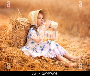 Un ritratto di una ragazza felice in un campo di grano al tramonto. Un bambino tiene in mano un vasetto di vetro con latte sullo sfondo delle orecchie di segale. Picnic nella natura. Foto Stock