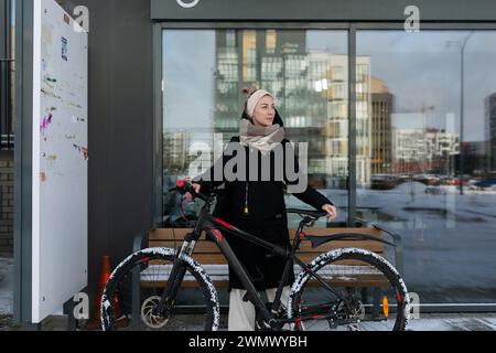 Una donna sorridente con dreadlock biondi ha noleggiato una bicicletta in inverno Foto Stock