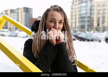 Una donna sorridente con dreadlock biondi cammina per la città con la neve in inverno Foto Stock