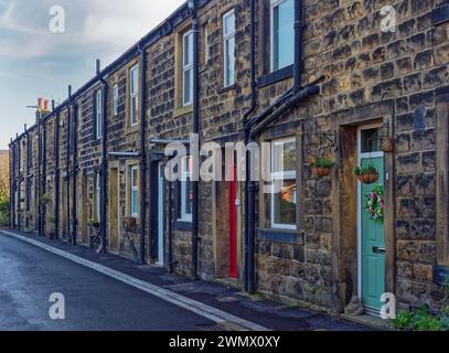 Una fila di tradizionali case a schiera dello Yorkshire su una strada stretta nei sobborghi di Otley, con porte anteriori colorate e cesti sospesi. Foto Stock