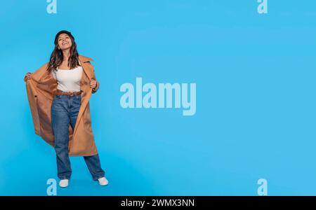 donna in jeans, maglietta bianca e cappotto marrone che danzano su sfondo blu. Gente felice Foto Stock