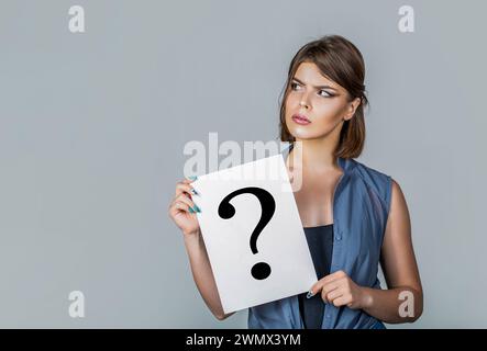 Donna che tiene un cartello con il simbolo del punto interrogativo, pensa. Domanda femminile. Donna con un'espressione dubbiosa e punti interrogativi. Donna pensante. Ottenere Foto Stock