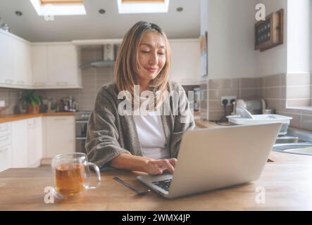 Donna asiatica che trascorre il tempo a casa bevendo caffè, tè, ascoltando musica, utilizzando un computer portatile, comunicando con la famiglia. Concetto di stile di vita Foto Stock