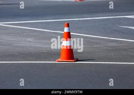 Un cono stradale arancione sulla strada. Il cono si trova in mezzo alla strada, per segnalare il pericolo. Il cono è realizzato in plastica e ha una calce trapezoidale Foto Stock