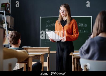 Una giovane insegnante caucasica che spiega la teoria della musica ai bambini durante la lezione Foto Stock