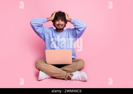 Foto di un ragazzo nervoso che siede per pavimento indossa abiti blu alla moda omg stress error error isolato su sfondo di colore rosa Foto Stock