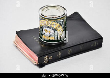 Una scatola di sciroppo d'oro di Lyle seduta in cima a un'antica bibbia sacra ricoperta di nero su sfondo bianco Foto Stock