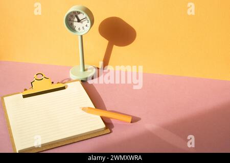 Portadocumenti e matita colorata, orologio sulla scrivania rosa. sfondo arancione della parete. area di lavoro Foto Stock
