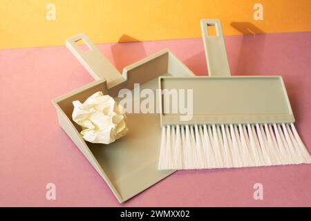 Spazzola in plastica grigia con paletta su pavimento rosa. sfondo arancione della parete Foto Stock