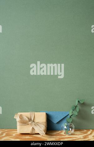 Confezione regalo in carta kraft, busta blu, eucalipto su tavolo in legno. sfondo verde della parete Foto Stock