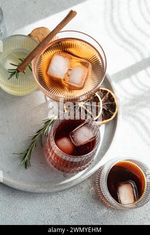 Dall'alto di bevande alcoliche assortite in bicchieri testurizzati, guarniti con cannella, rosmarino e agrumi secchi, su un vassoio rotondo Foto Stock