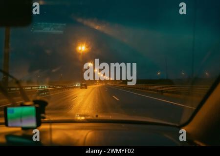 superstrada notturna. Segnali stradali. una vista dall'interno di un'auto a piedi. Guida pericolosa. spazzole tergicristalli funzionanti. Gocce di pioggia sul parabrezza dell'auto. diffi Foto Stock