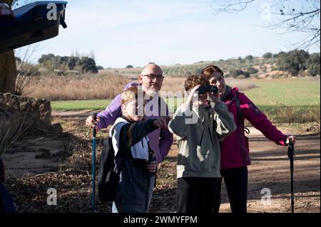 Una famiglia allegra che si gode una giornata di sole facendo escursioni in campagna, con due bambini sorridenti, uno con pali da trekking e l'altro con la binocula Foto Stock
