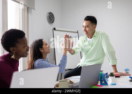 Tre colleghi condividono un massimo di cinque in un ufficio, celebrando il successo con sorrisi ed entusiasmo. Foto Stock