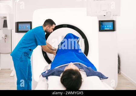 Radiologo maschio sorridente che utilizza un computer mentre prepara una paziente femminile per una scansione tomografica computerizzata in una moderna struttura medica. Foto Stock