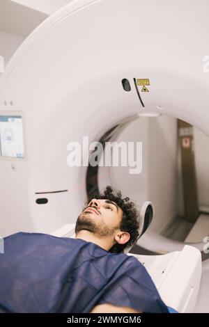 Un giovane paziente di sesso maschile si trova in uno scanner TC durante una procedura di imaging medico, con particolare attenzione alla tecnologia sanitaria avanzata. Foto Stock