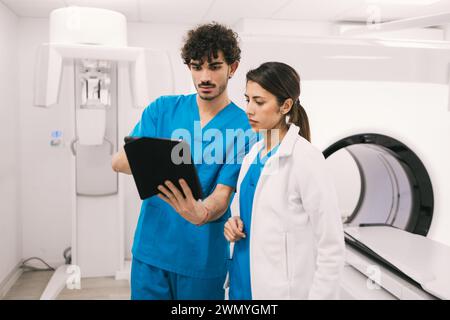 Due operatori sanitari, un maschio in scrub e una femmina in un camice da laboratorio, stanno intensamente rivedendo una tavoletta digitale in un ambiente ospedaliero moderno, possibilmente ne Foto Stock