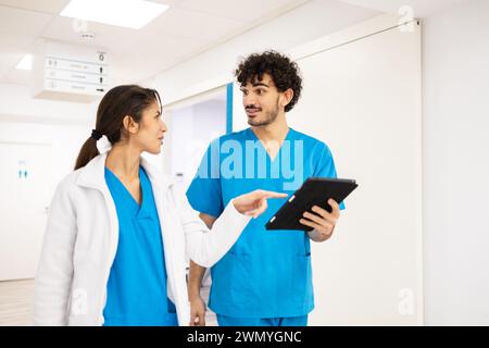Due professionisti sanitari discutono dell'assistenza al paziente mentre camminano in un corridoio ospedaliero Foto Stock