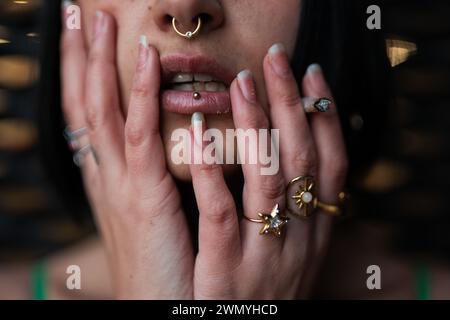 Un primo piano dettagliato di un labbro inferiore perforato e anelli decorati di una donna che rispecchiano uno stile urbano moderno. Foto Stock