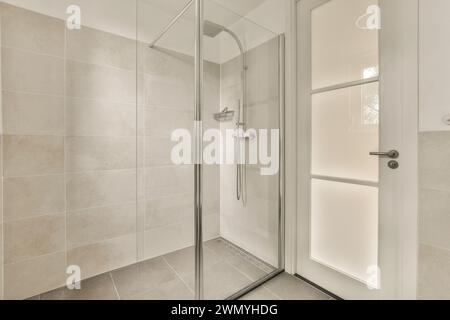 Un bagno pulito e moderno con cabina doccia in vetro e pareti piastrellate di beige. Foto Stock