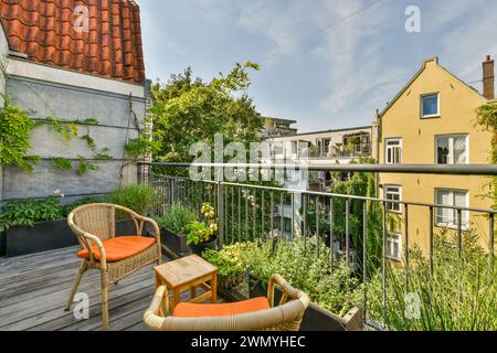 Un pittoresco balcone urbano adornato con piante verdi e comodi mobili in vimini sotto un cielo azzurro. Foto Stock