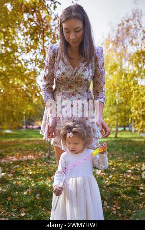 Una madre etnica guida la sua giovane figlia mentre trascorrono del tempo insieme in un parco illuminato dal sole pieno di colori autunnali in California, Stati Uniti. Foto Stock