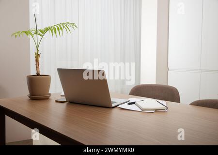 Computer portatile e vaso di fiori su un tavolo di legno all'interno di casa Foto Stock