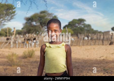 bambino di villaggio africano su una strada sterrata , kraal con piccoli animali che pascolano sullo sfondo, Foto Stock