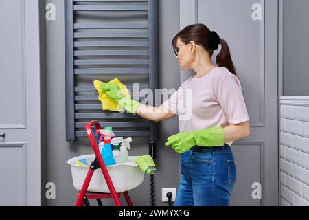 Donna che pulisce la casa in bagno, pulisce la polvere dal portasciugamani riscaldato Foto Stock