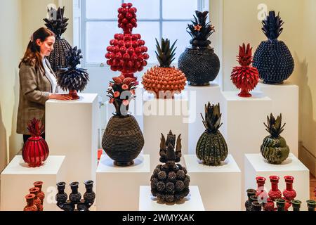 Londra, Regno Unito. 28 febbraio 2024. Un rappresentante della galleria per Objekti Collectable Art con una collezione di pezzi di ceramica a forma di ananas dell'artista messicano Pedro Hernández Carlos. Collect 2024 celebra i 20 anni come fiera internazionale leader per l'artigianato e il design contemporaneo. È presentato dal Crafts Council alla Somerset House dal 1 al 3 marzo, con 40 gallerie internazionali e opere di oltre 400 artisti viventi. Crediti: Imageplotter/Alamy Live News Foto Stock