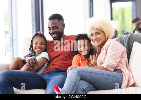 Padre afroamericano, madre birazziale, figlia e figlio sorridono su un divano Foto Stock