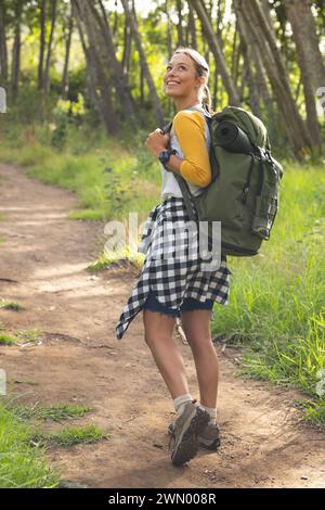 La giovane donna caucasica si diverte a fare un'escursione in una foresta illuminata dal sole Foto Stock