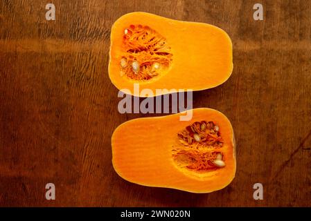 Due metà di fette di zucca matura butternut a fette con semi su rustico piano in legno dall'alto Foto Stock