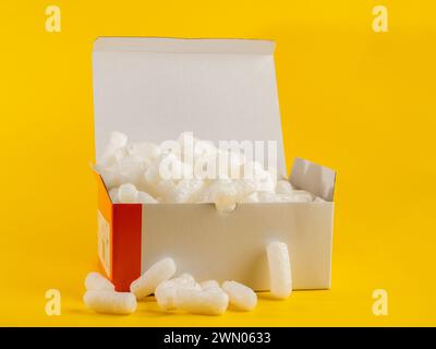 Arachidi da imballaggio bianche in un cartone da imballaggio isolato su sfondo giallo Foto Stock