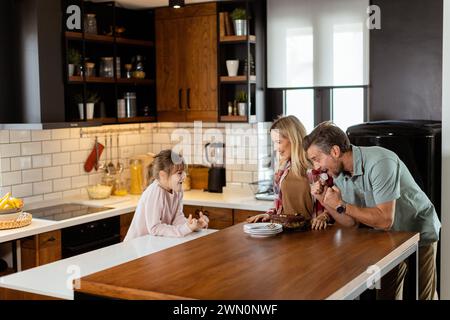 Una scena emozionante si svolge mentre una famiglia assaggia insieme una deliziosa torta al cioccolato nel calore della sua cucina soleggiata, condividendo sorrisi e sorrisi Foto Stock