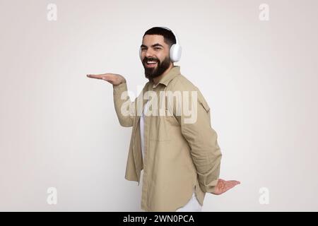 Esuberante uomo barbuto con un ampio sorriso, con cuffie bianche e una camicia beige Foto Stock