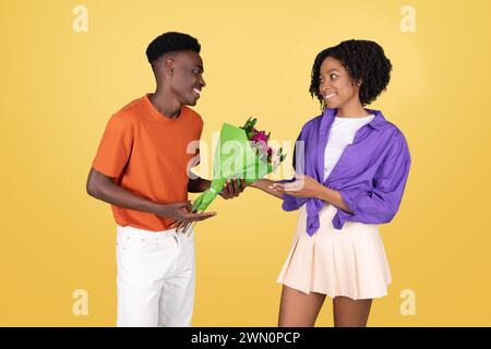 Un giovane con una camicia arancione regala un mazzo di fiori avvolti in carta verde a una giovane donna felice Foto Stock