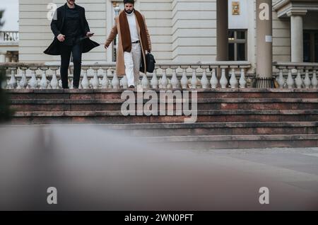 Colleghi professionisti in un abbigliamento elegante che lasciano un edificio di uffici, catturati mentre scendono le scale all'aperto in un ambiente urbano. Foto Stock