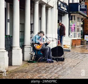 Un busker/artista di strada con una chitarra sulla strada principale nella città mercato di Marlborough Wiltshire Regno Unito Foto Stock