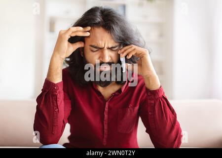 L'uomo indiano millenario barbuto turbato ha una conversazione telefonica a casa Foto Stock