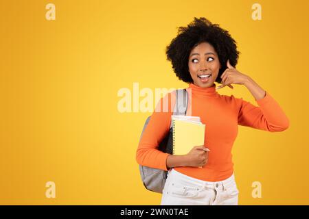 Divertita giovane donna con i capelli afro, in un maglione arancione e pantaloni bianchi Foto Stock