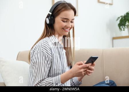 Giovane donna con cuffie e smartphone sul divano di casa Foto Stock