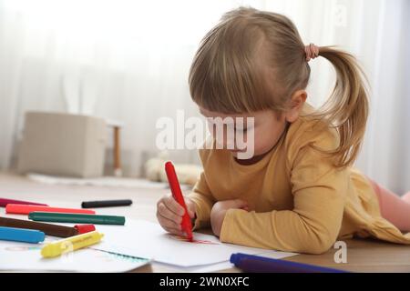 Bella bambina che disegna con un pennarello sul pavimento in interni. Arte dei bambini Foto Stock