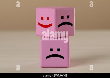 Cubi rosa con volti tristi e felici su un tavolo di legno Foto Stock