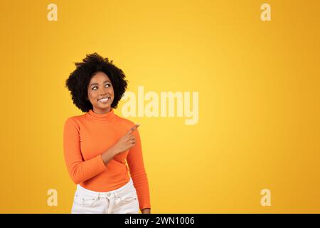 Una giovane donna sorridente con i capelli afro punta a qualcosa fuori dalla macchina fotografica Foto Stock