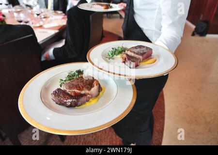 Primo piano di un cameriere che porta piatti di bistecche di filetto di manzo su piatti in un ristorante elegante Foto Stock
