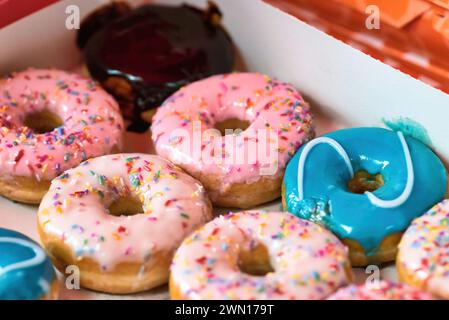 Primo piano di una scatola di cartone piena di ciambelle colorate ricoperte di cospargimenti e glassa di zucchero Foto Stock