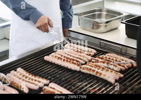 Primo piano di un uomo che trasforma salsicce bratwurst su un barbecue con un paio di pinze Foto Stock