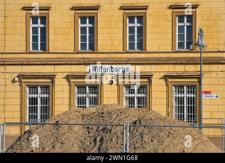 Wittenberge, Germania. 28 febbraio 2024. Un mucchio di sabbia si trova dietro una recinzione metallica di fronte all'edificio della stazione ferroviaria di Wittenberge. La città sull'Elba a Prignitz diventerà la sede della prima accademia cittadina tedesca. La Small Town Academy è una piattaforma di networking e conoscenza a livello nazionale per le piccole città in Germania. L'ufficio si sposterà nelle stanze dell'edificio storico della stazione ferroviaria, che è attualmente in fase di ristrutturazione. Credito: Soeren Stache/dpa/Alamy Live News Foto Stock